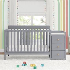 a baby's room with a crib, dresser and toy blocks in front of the window