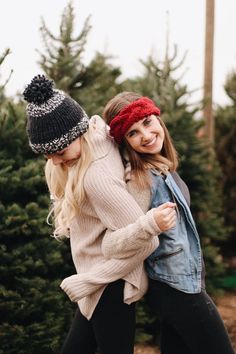 two young women hugging each other in front of christmas trees