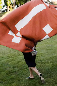 a woman carrying a large red and white flag on top of a lush green field