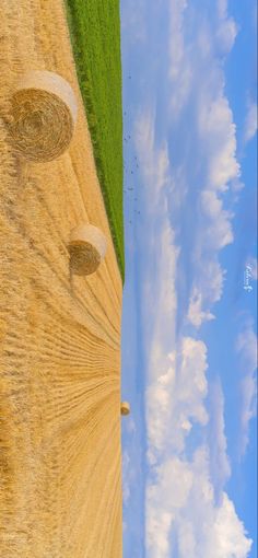 two round bales in the middle of a field with blue sky and white clouds