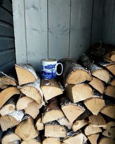 a stack of firewood with a mug on it sitting in front of the pile