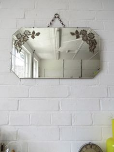 a mirror hanging on the side of a white brick wall next to a clock and vase