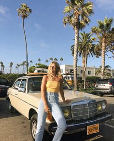 a woman leaning on the hood of a car in a parking lot with palm trees