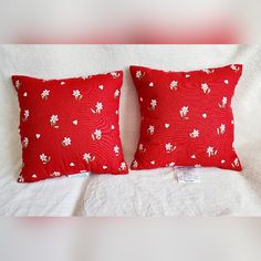 two red pillows sitting on top of a bed next to each other in front of a white wall