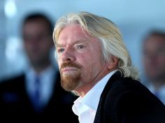 a man with blonde hair and beard standing in front of other men wearing black suits