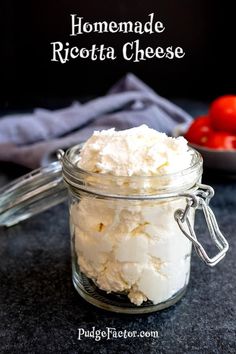 homemade ricotta cheese in a small glass jar on a counter with tomatoes behind it