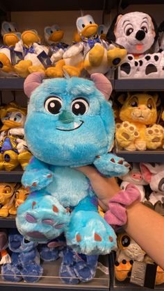 a person is holding a blue stuffed animal in front of shelves with other stuffed animals