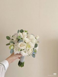 a person holding a bouquet of white and green flowers in front of a beige wall