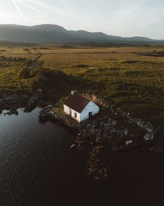 an aerial view of a small house in the middle of a body of water with mountains in the background