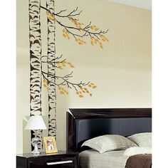 a bed room with a neatly made bed and a tree decal on the wall