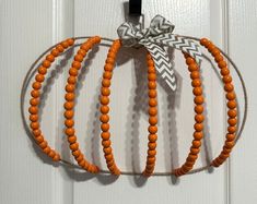 an orange beaded pumpkin hanging on a door with a ribbon around it's neck