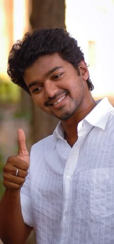 a man giving the thumbs up sign in front of his face and wearing a white shirt