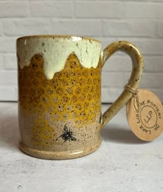 a yellow and white coffee mug with a bee on the inside is next to a tag