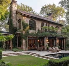 a large stone house with lots of greenery on the front and side walls, surrounded by lush green trees