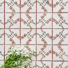 a vase filled with flowers sitting on top of a tile wall covered in orange and white tiles