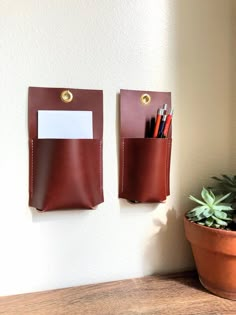 two leather pockets hold pens, pencils and other office supplies next to a potted plant