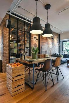 an open concept living room and dining area with wood flooring, exposed brick wall, black pendant lights over the table