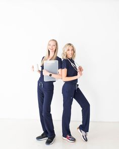 two women in scrubs are holding laptops and posing for the camera with their arms around each other