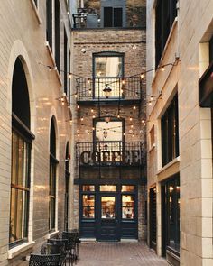 an alley way with tables and chairs on the sidewalk in front of tall brick buildings