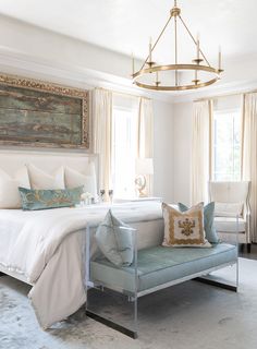 a bedroom with a bed, chair and chandelier hanging from the ceiling in front of two windows