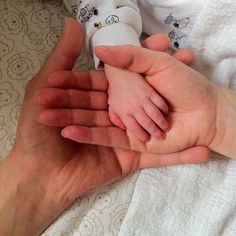 a person holding a baby's hand while laying on top of a white blanket