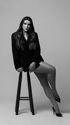 a woman sitting on top of a stool wearing high heels and a black shirt with long sleeves