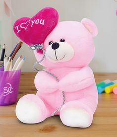 a pink teddy bear sitting on top of a wooden table next to pencils and markers