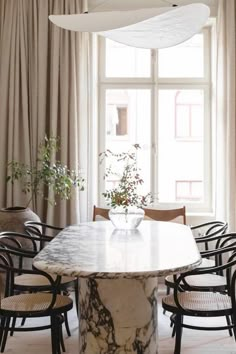 a dining room table with chairs and a vase on it in front of a window