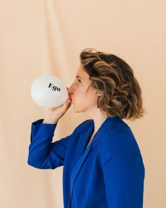 a woman in a blue jacket is holding a white frisbee to her mouth