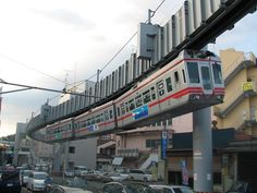 a train traveling over a street next to tall buildings and parked cars in front of it