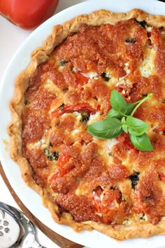 a tomato and basil quiche on a white plate next to two tomatoes, one with green leaves