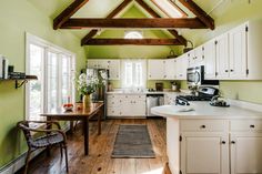 a kitchen with green walls and white cabinets, wood flooring and an open beamed ceiling