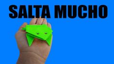 a hand holding an origami frog with the words salta mucho above it