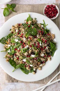 a white plate topped with spinach and feta salad next to a bowl of pomegranate