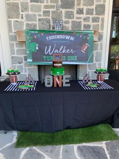 a table topped with football themed items and decorations for a gameday party in front of a stone building