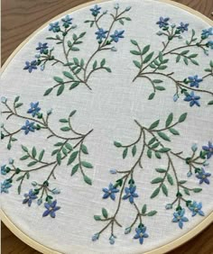 a close up of a embroidery on a wooden table with blue flowers and green leaves