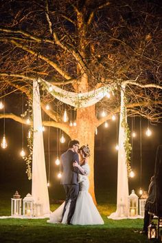 a bride and groom standing in front of a tree with lights strung from the branches