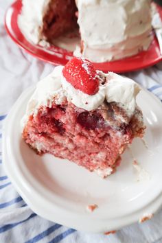 a piece of strawberry cake with white frosting on a plate next to another slice