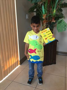 a young boy holding up a book in front of a potted plant and door