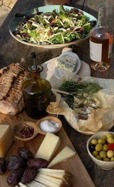 an assortment of cheeses, olives and bread on a picnic table