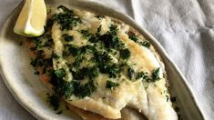 a white plate topped with fish covered in cheese and spinach next to a lemon wedge