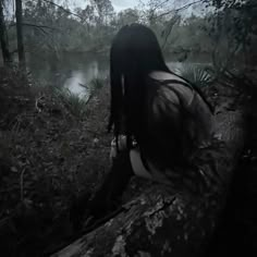 a woman with long hair sitting on a log in the woods looking out over a lake