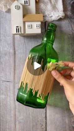 a person holding a green bottle over a wooden table with doll houses on the side