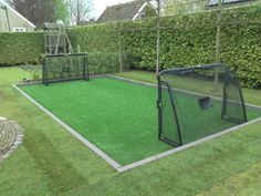 a backyard with artificial turf and a batting cage in the center, surrounded by hedges