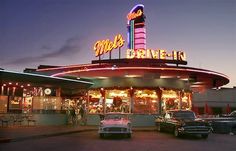 cars parked in front of a drive - in movie theater at night with neon lights