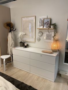 a white dresser sitting in a bedroom next to a window with pictures on the wall