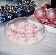 some pink flowers in a glass bowl on a white fur covered table next to silver ornaments