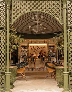 an outdoor dining area with wicker chairs and green trellis on the ceiling, surrounded by greenery