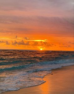 the sun is setting over the ocean with waves lapping in front of an orange and yellow sky