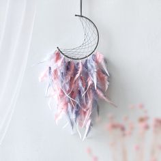 a pink and blue feather dream catcher hanging on a wall next to some dried flowers